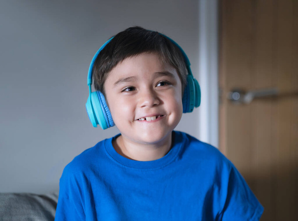 Портрет щасливої змішаної раси дитини в навушниках і дивлячись вгору з усміхненим обличчям, Щасливий маленький хлопчик в синій футболці прослуховування музики, милий малюк сидить на дивані, розслабляючись у вітальні вдома
 - Фото, зображення