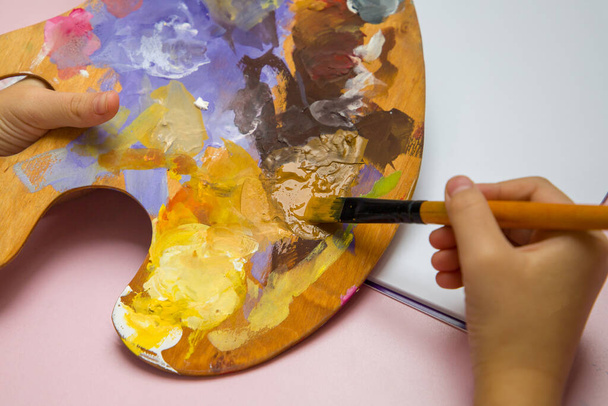 The child draws with a brush on a palette holding it. - Fotografie, Obrázek