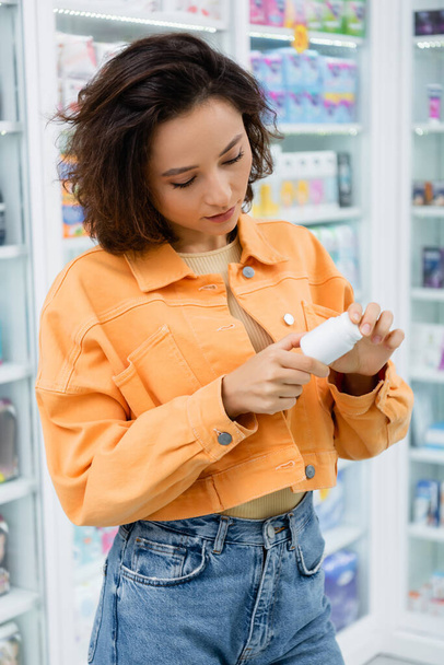 brunette customer looking at bottle with medication in drugstore  - Zdjęcie, obraz