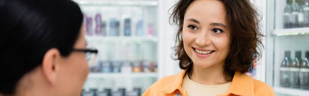 donna bruna sorridente mentre guarda il farmacista sfocato in farmacia, banner - Foto, immagini