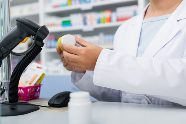 cropped view of pharmacist in white coat scanning bottle with medication at counter - Φωτογραφία, εικόνα