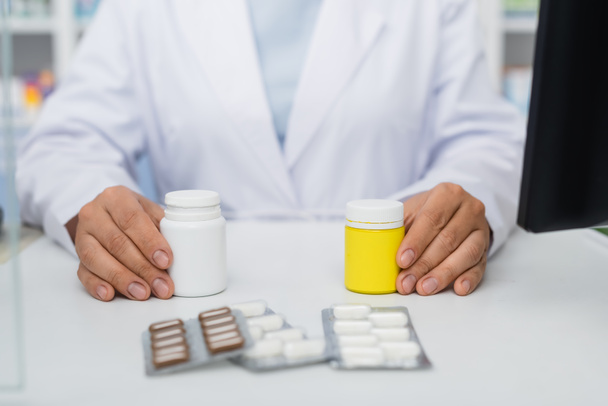 обрізаний вид фармацевта, який тримає пляшки з ліками біля блістерних пакетів
 - Фото, зображення