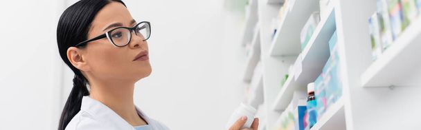 asian pharmacist in glasses looking at medication in drugstore, banner - Fotó, kép