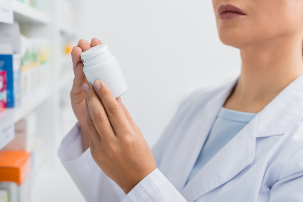 partial view of pharmacist in white coat holding bottle with medication - Foto, afbeelding