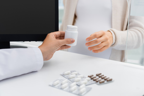 vista recortada del farmacéutico dando frasco con vitaminas a la mujer embarazada en el mostrador  - Foto, Imagen