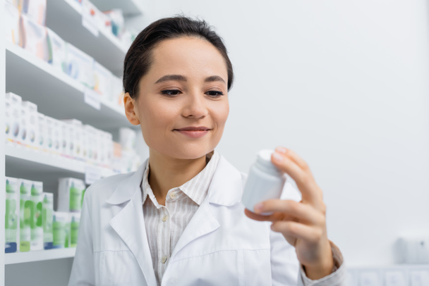 cheerful pharmacist in white coat holding bottle with medication  - Fotoğraf, Görsel