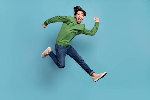 Full length photo of positive happy crazy man jump up good mood run empty space isolated on blue color background - Foto, afbeelding