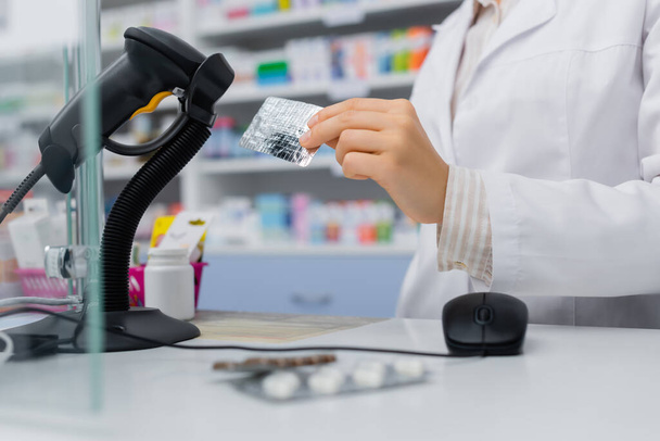 cropped view of pharmacist holding blister pack near scanner in drugstore - 写真・画像