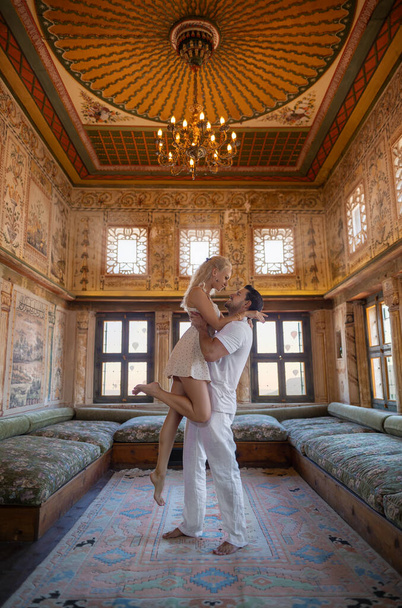 Couple man and woman hugs in a rich ancient historical ottoman hall in Cappadocia with flying balloons in the windows, Turkey. - Fotoğraf, Görsel