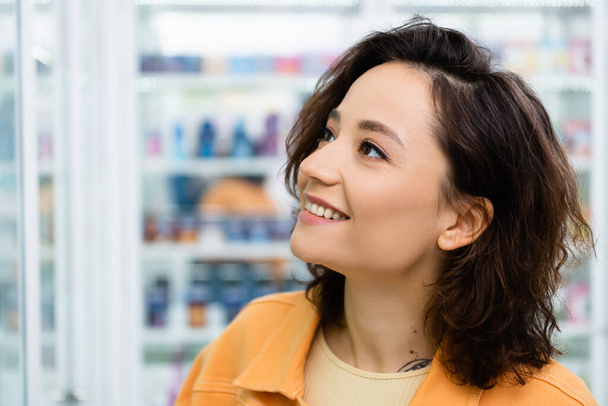 tattooed woman looking away and smiling in drugstore - Фото, зображення