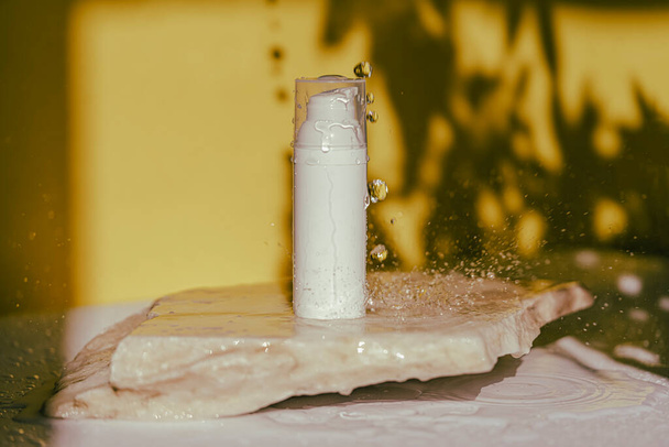 化粧品ボトルは石の上に立っている。水が落ちて影が残る黄色の背景に . - 写真・画像