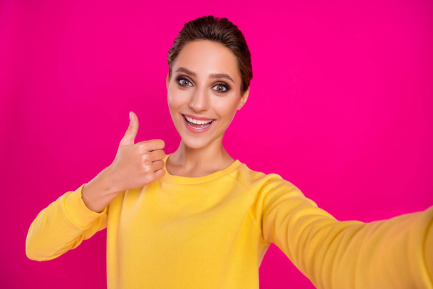 Photo of shiny excited young lady wear yellow jumper smiling tacking selfie showing thumb up isolated pink color background - Photo, Image