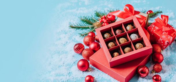 Chocolates en una caja roja festiva trufa de chocolate negro en un fondo de Navidad con pelotas de Año Nuevo ramas de abeto. plano simulan espacio de copia. - Foto, Imagen