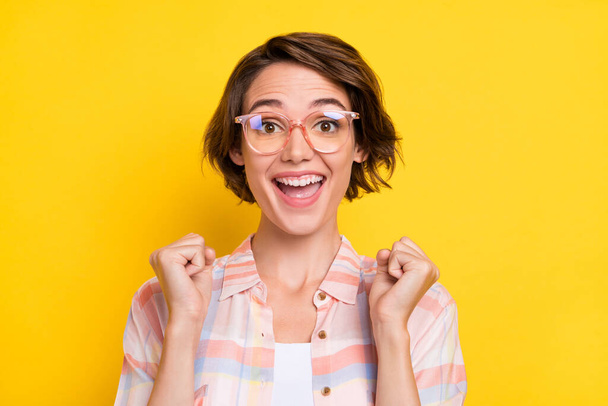 Photo of amazed shocked happy young woman raise fists winner cool wear glasses isolated on yellow color background - Foto, Imagem
