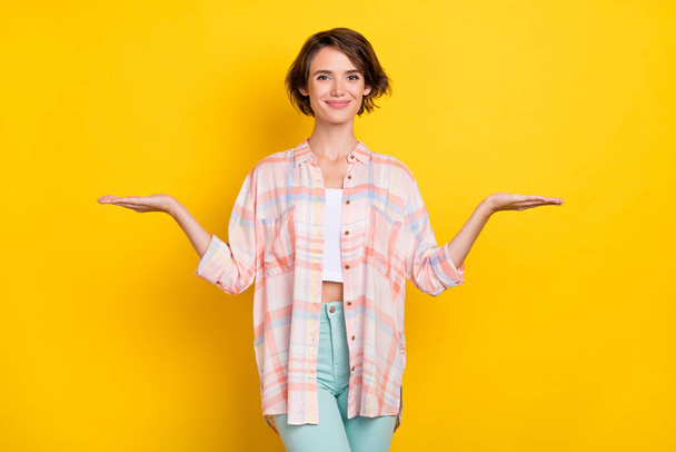 Portrait of attractive cheerful girl holding on palms copy blank space ad isolated over vivid yellow color background - Foto, Imagem