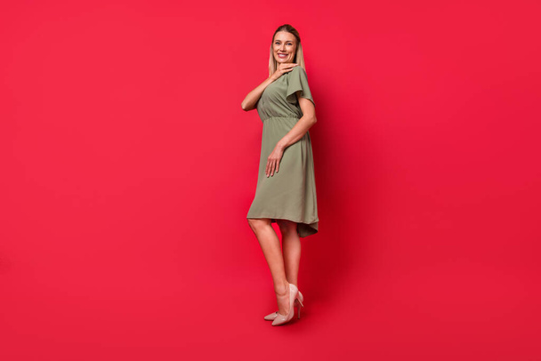 Photo of adorable sweet young lady wear green outfit smiling walking high heels isolated red color background - Фото, зображення