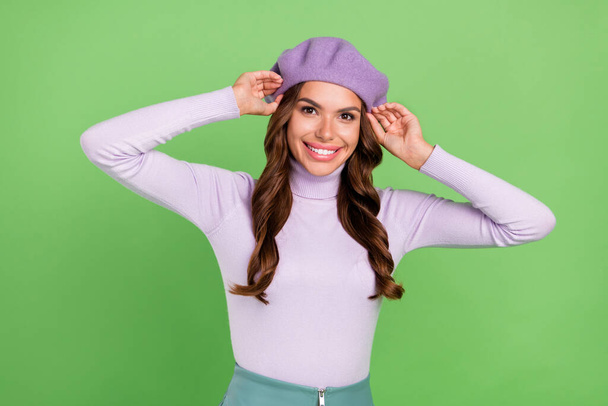 Photo of adorable satisfied girl hands touch headwear beaming smile look camera isolated on green color background - Valokuva, kuva