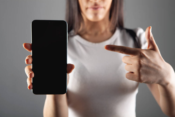 young woman shows phone on gray background - Fotoğraf, Görsel