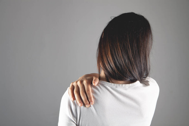 mujer tiene dolor de hombro sobre fondo gris - Foto, Imagen