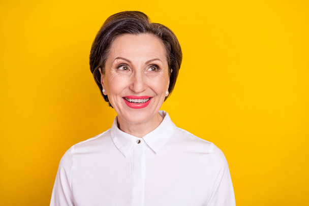 Photo of charming sweet age woman dressed white shirt smiling looking empty space isolated yellow color background - Fotoğraf, Görsel