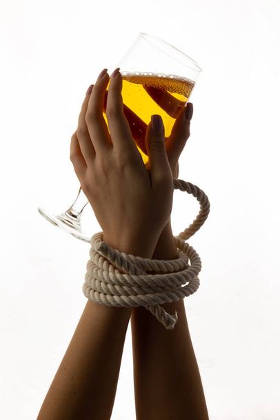 Gefesselte weibliche Hände halten ein Glas mit Alkohol auf weißem Hintergrund. - Foto, Bild