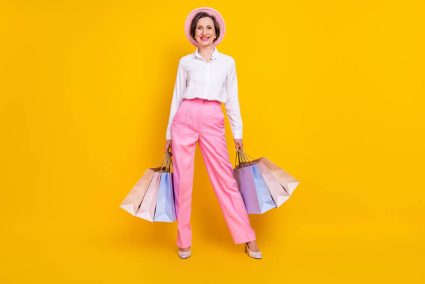 Full length photo of aged woman happy positive smile hold bags shop customer sale isolated over yellow color background - Foto, Imagen