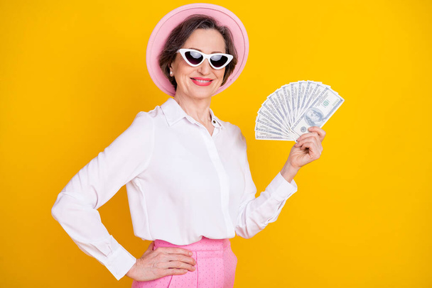 Profile side photo of aged rich woman happy positive smile hold money cash dollars isolated over yellow color background - Foto, Imagem
