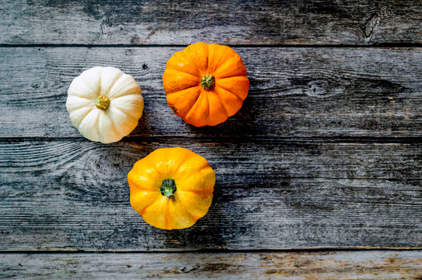 Three decorative mini pumpkins on a rustic wooden background. Colorful autumn scene for restaurants, cooking recipes, Thanksgiving or Halloween. Top view, flat lay, copy space. - Foto, Bild