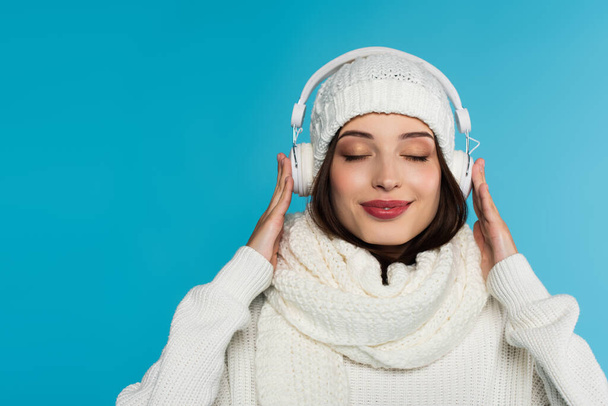 Young woman in headphones and scarf listening music in headphones with closed eyes isolated on blue  - Photo, Image