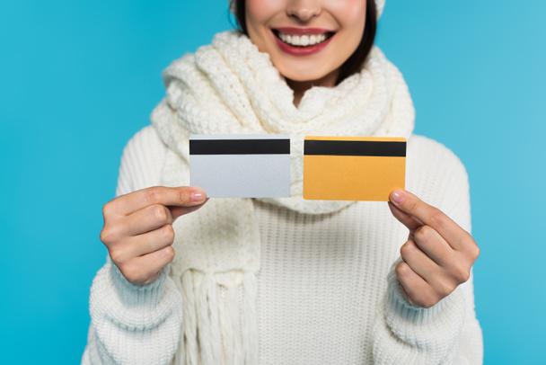 Vista recortada de la mujer borrosa en suéter de punto con tarjetas de crédito aisladas en azul  - Foto, imagen