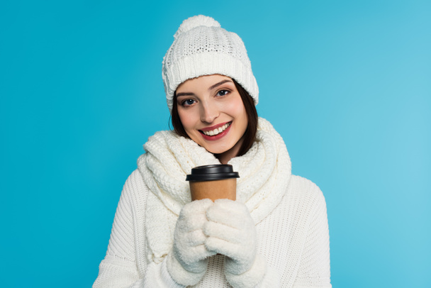 Positive woman in gloves and warm scarf holding paper cup isolated on blue  - Foto, Imagen