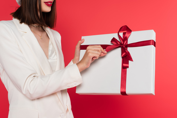 Cropped view of woman with red lips holding present isolated on red  - Фото, изображение