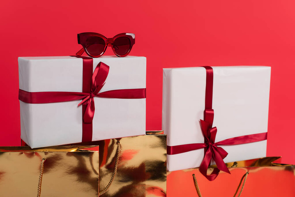 Sunglasses on present near shopping bags isolated on red  - Photo, Image