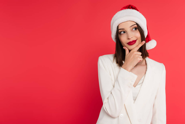 Frau mit Weihnachtsmütze und weißer Jacke vereinzelt auf Rot  - Foto, Bild
