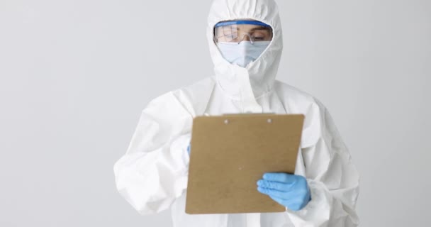 Medico in tuta protettiva anti-peste scrittura in documenti e mostrando pollice su film 4k - Filmati, video