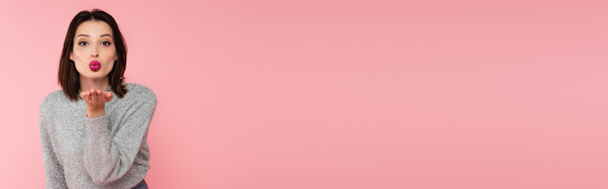 Bella donna in maglione che soffia aria bacio alla fotocamera isolata su rosa, banner  - Foto, immagini