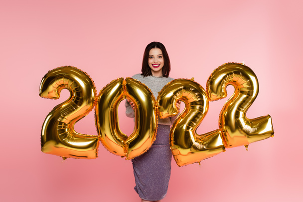 Happy stylish woman standing near balloons in shape of 2022 numbers isolated on pink  - Foto, Imagem