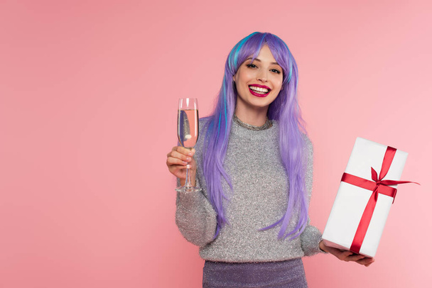 Stylish woman with dyed hair holding champagne and gift box isolated on pink  - Fotó, kép