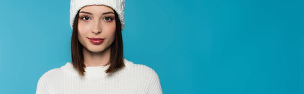 Brunette woman in knitted hat and sweater looking at camera isolated on blue, banner  - Foto, imagen
