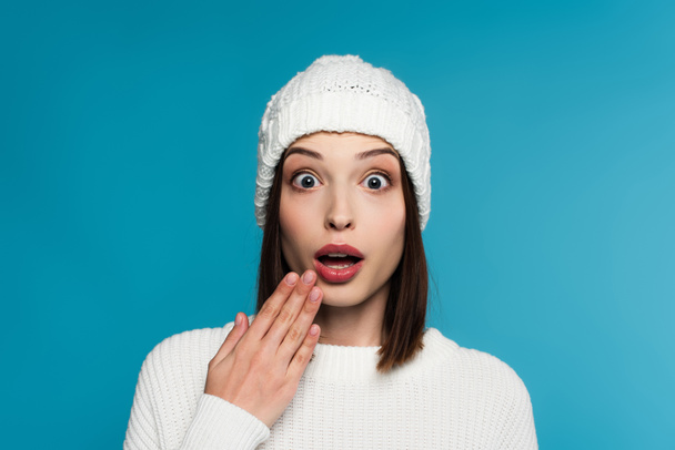 Amazed woman in white hat and sweater looking at camera isolated on blue  - Foto, Imagem