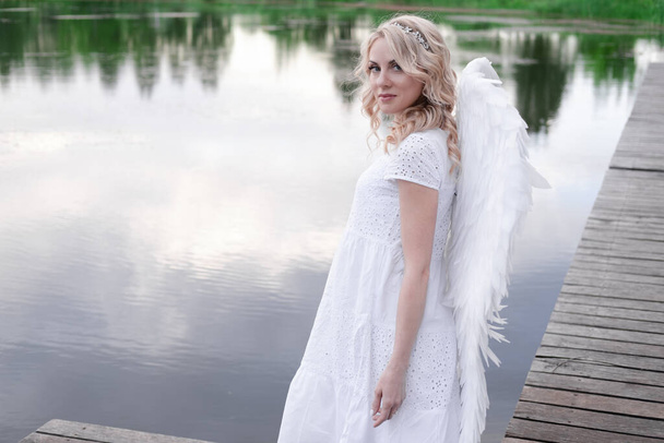 白い天使の翼を持つ女性。天使の衣装を着た美しいブロンド。天国、純度。いい人だ. - 写真・画像