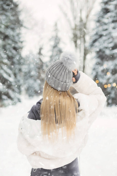 Beautiful blond woman in a white coat looking to the forest in snowy weather - Photo, Image
