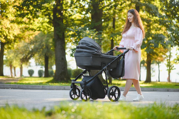 family, child and parenthood concept - happy mother walking with baby stroller in park. - Φωτογραφία, εικόνα