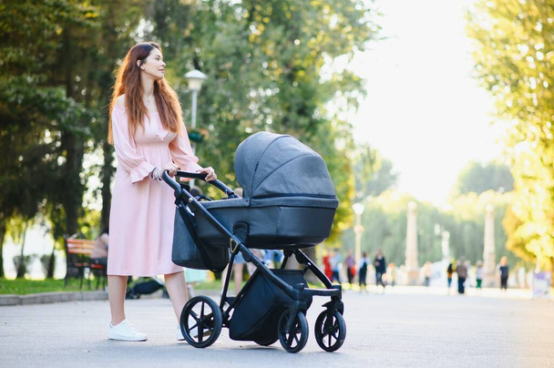 Happy young mother with baby in buggy walking in autumn park - Foto, afbeelding