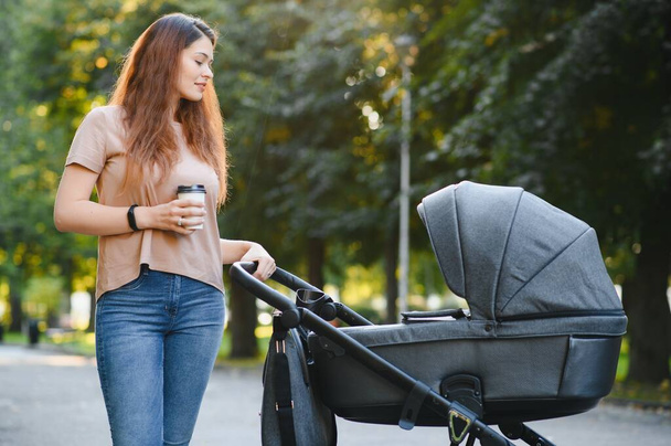 beautiful and young woman mother and baby in a stroller walking in the park - Foto, Bild