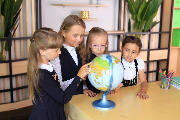 Dzieci w szkolnych mundurkach z globusem w biurze. - Zdjęcie, obraz