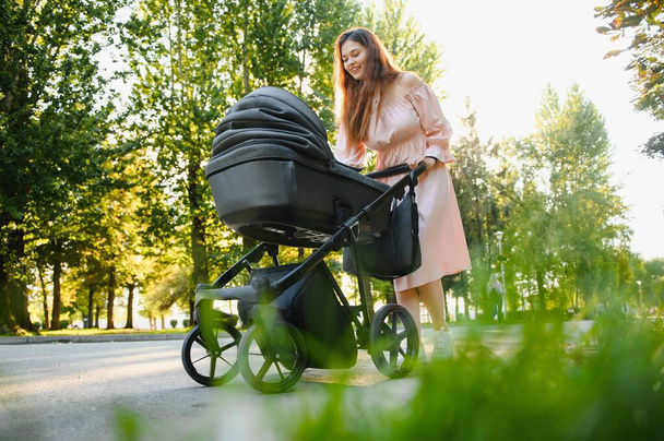 Happy young mother with baby in buggy walking in autumn park - Фото, изображение