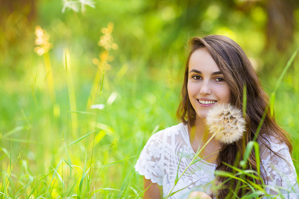Happy young beautiful woman sitting on grass with dandelion flow - Foto, imagen