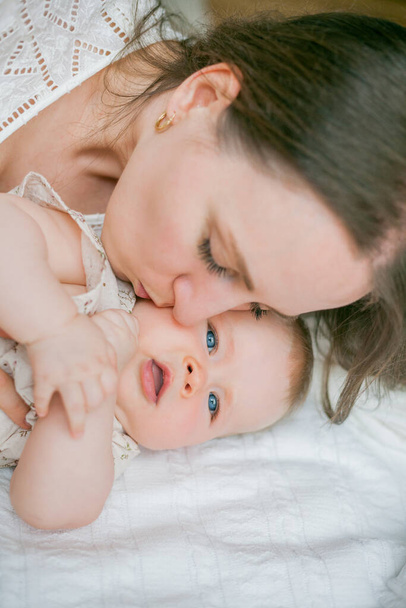 Šťastná mladá matka drží její malou dceru 5 měsíců ve svém náručí, zatímco leží na posteli. - Fotografie, Obrázek
