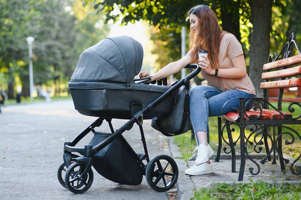 Happy young mother with baby in buggy sitting on bench in autumn park - Foto, Imagen